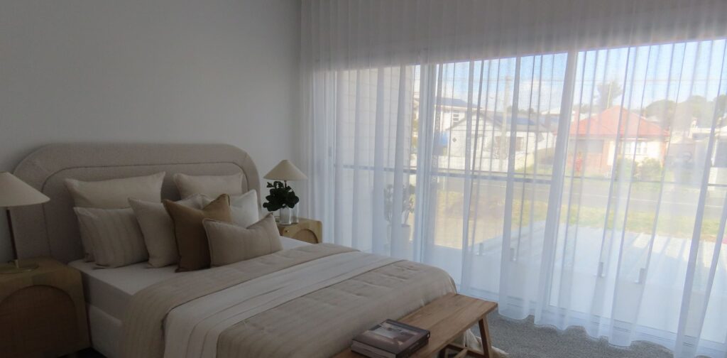 A large window with a view of a suburban streetscape is covered by floor-to-ceiling sheer white S-fold curtains.