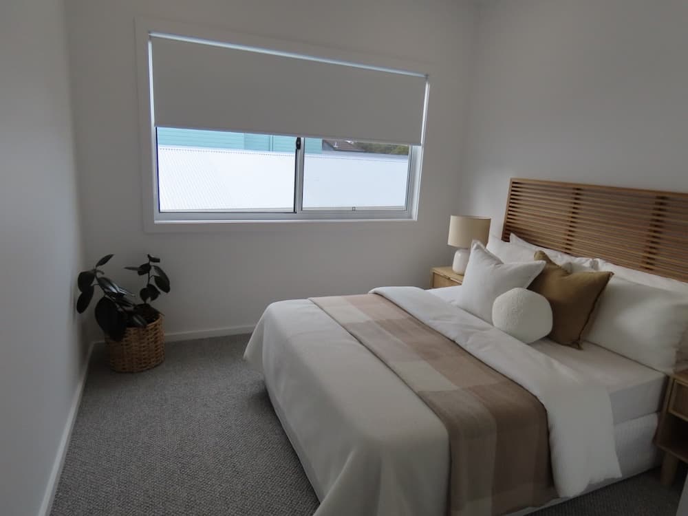 A window covered by a white blockout roller blind, partially lowered.