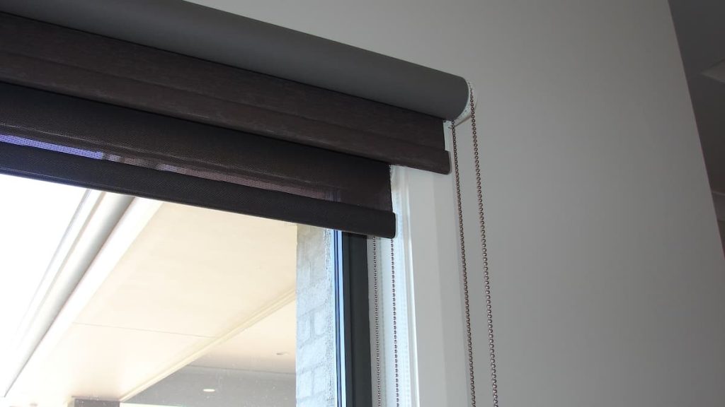 A close-up view of a window fitted with dark grey double roller blinds