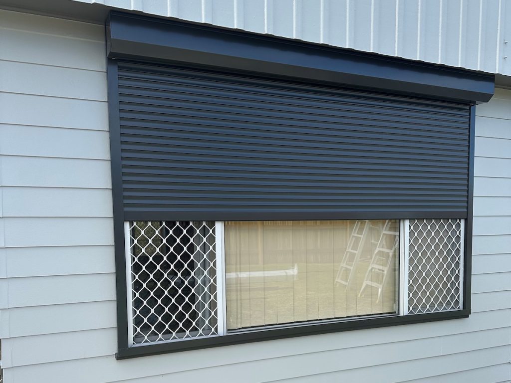 A black external roller shutter is partially lowered over a window.