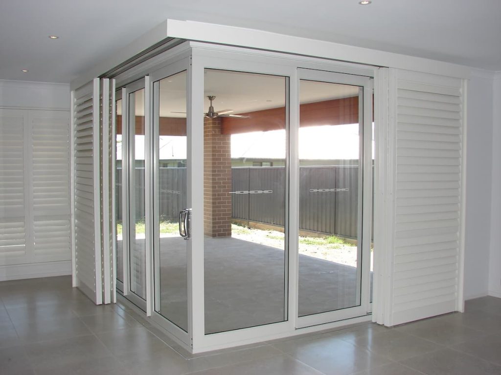 The doors are flanked on both sides by white bi-fold plantation shutters that are currently stacked back, leaving the door opening clear.