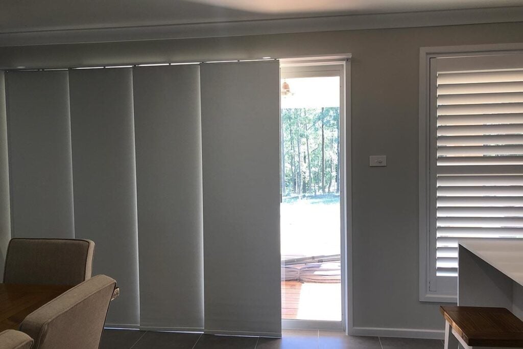 A large sliding door is fitted with pale grey panel glide blinds